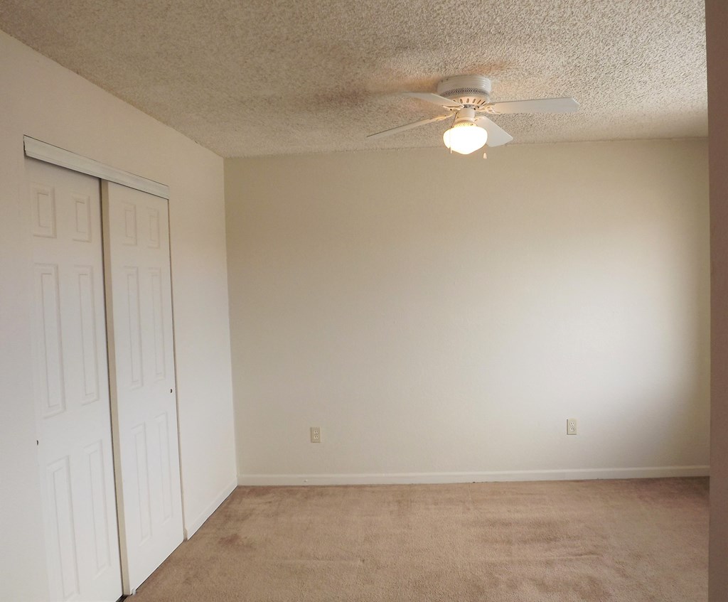 an empty living room with a ceiling fan and a closet