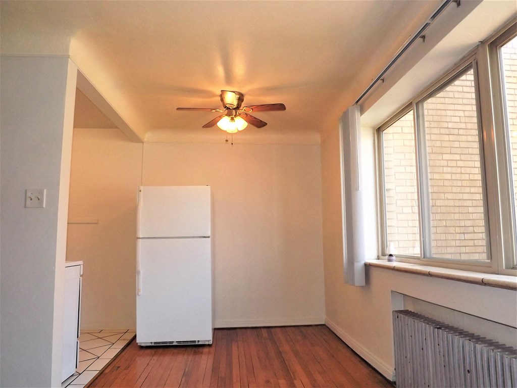 an empty living room with a ceiling fan and a refrigerator