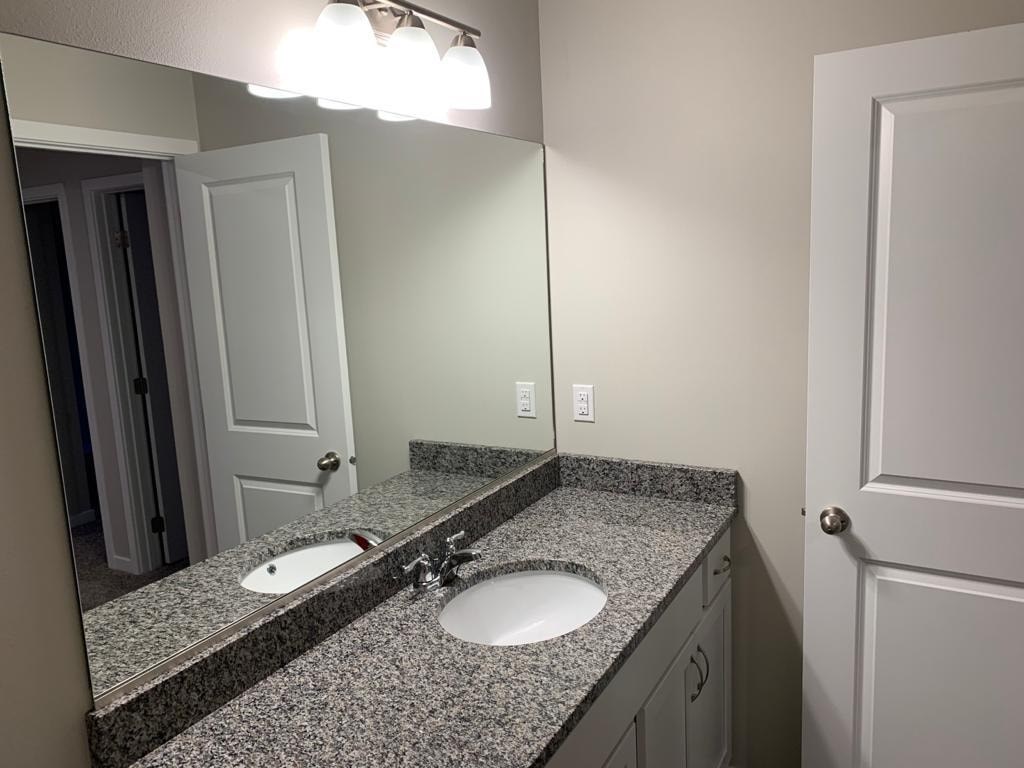 A bathroom with a granite countertop and a double sink.
