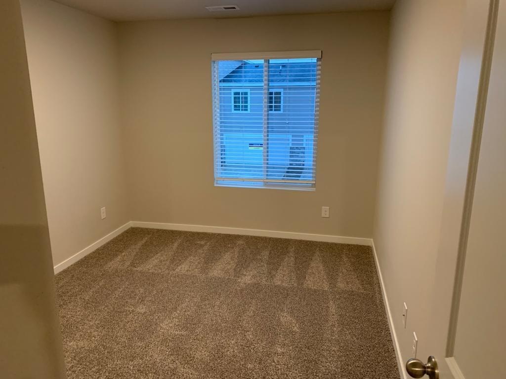 A room with a carpeted floor and a window with blinds.