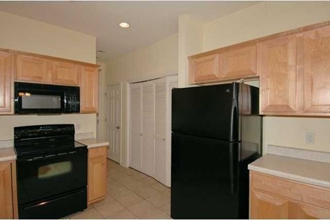 A black refrigerator stands in a kitchen with wooden cabinets.