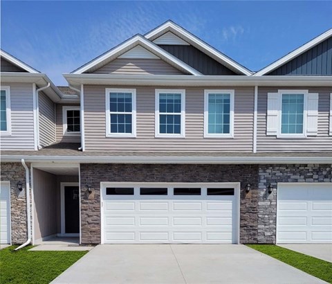 A modern house with a stone wall and two white garage doors.