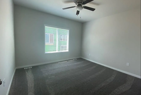 A room with a ceiling fan and a window showing a building outside.