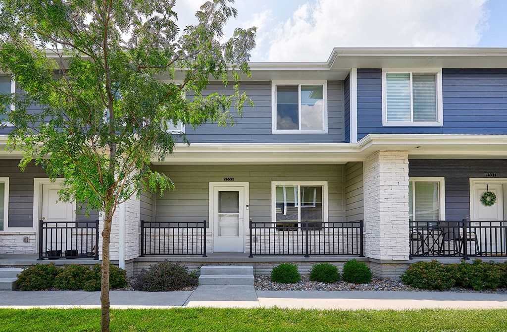 A two-story house with a front porch and a tree in front.