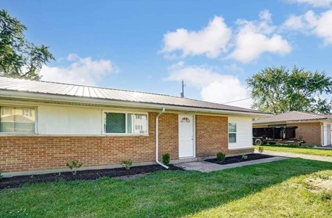 A house with a white door and windows is surrounded by a green lawn.
