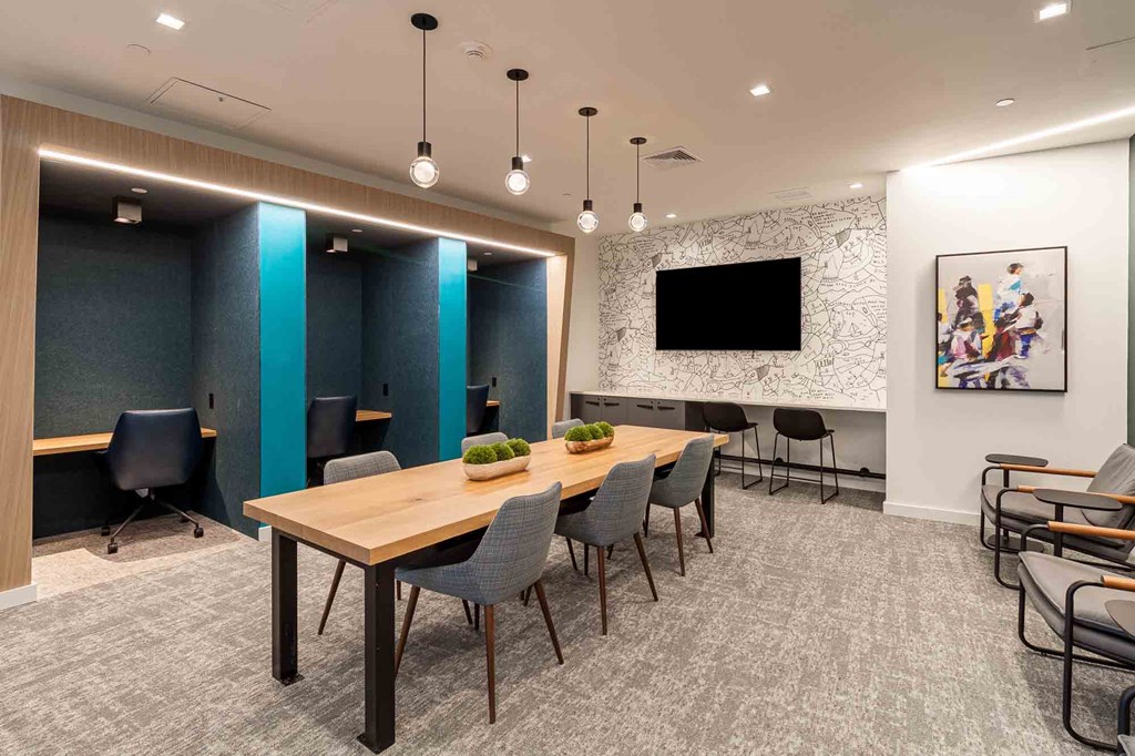 A conference room with a long table and chairs, a television, and a painting on the wall.