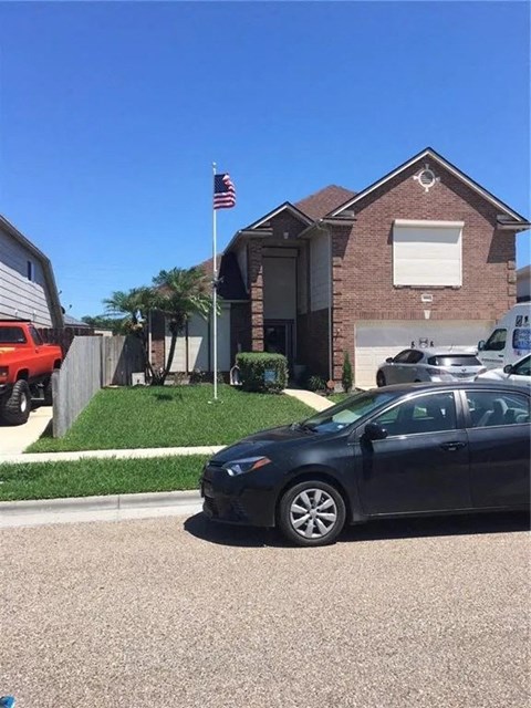 A black car is parked in front of a house with a flag on the roof.
