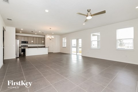 A spacious living room with a kitchen in the background and a ceiling fan above.