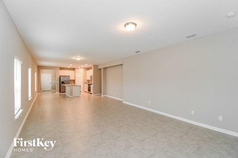 an empty living room with a kitchen in the background