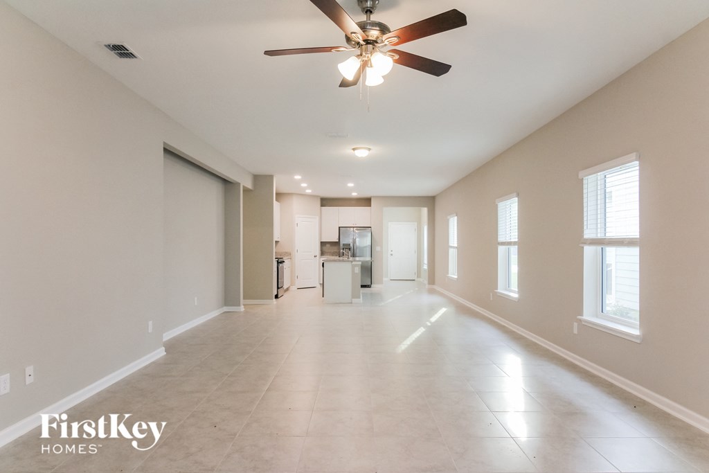 an empty living room with a ceiling fan and a kitchen