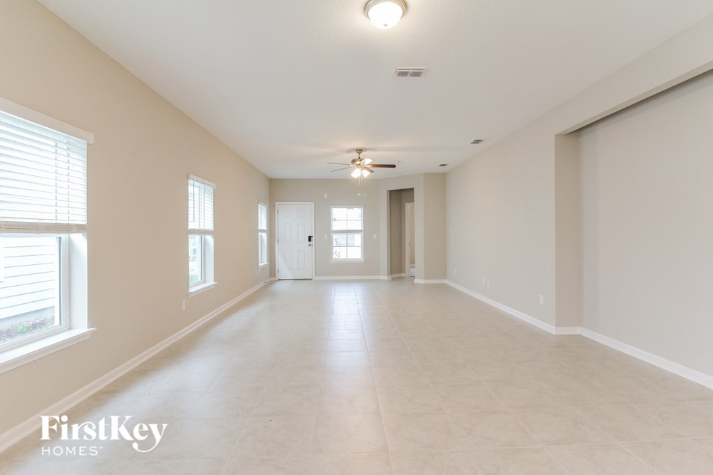 an empty living room with a ceiling fan and large windows