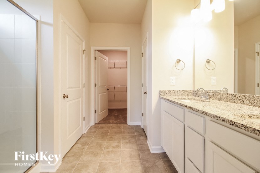a bathroom with white cabinets and a sink and a hallway to a closet