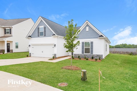 A house with a white and grey exterior is shown with a tree in the front yard.