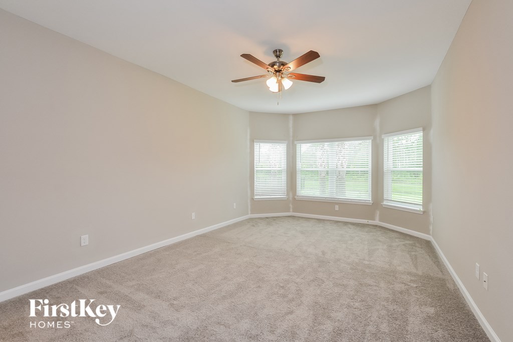 an empty living room with a ceiling fan and large windows