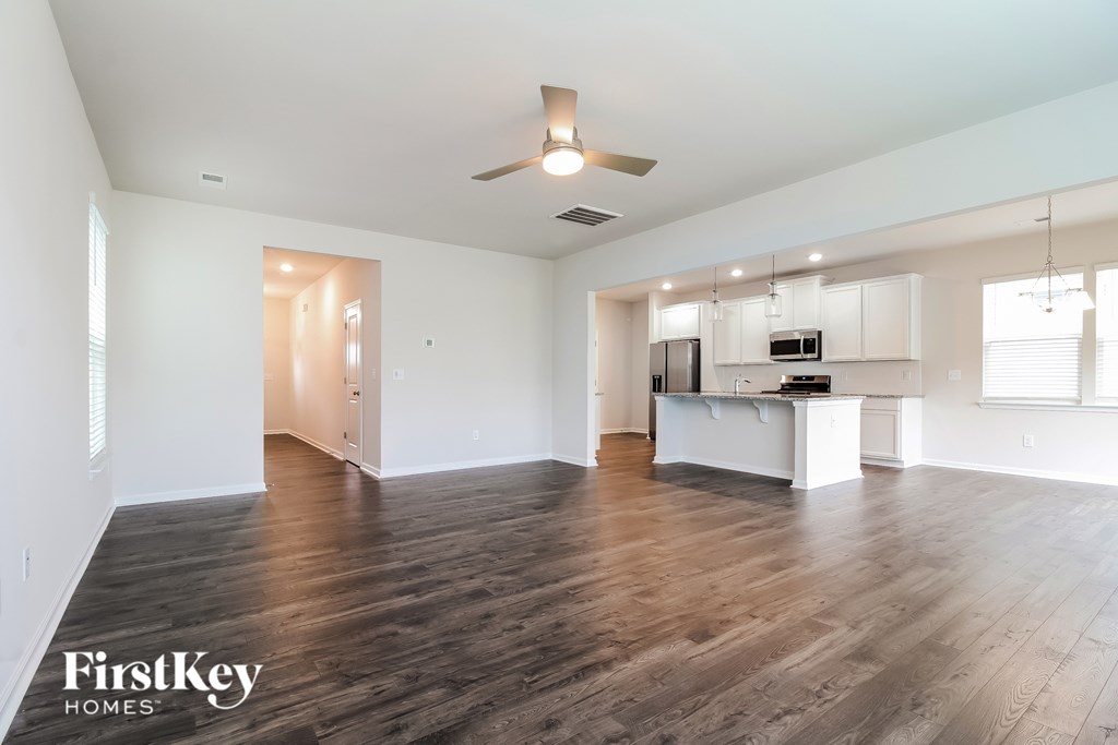 A spacious living room with a kitchen in the background and a ceiling fan above.