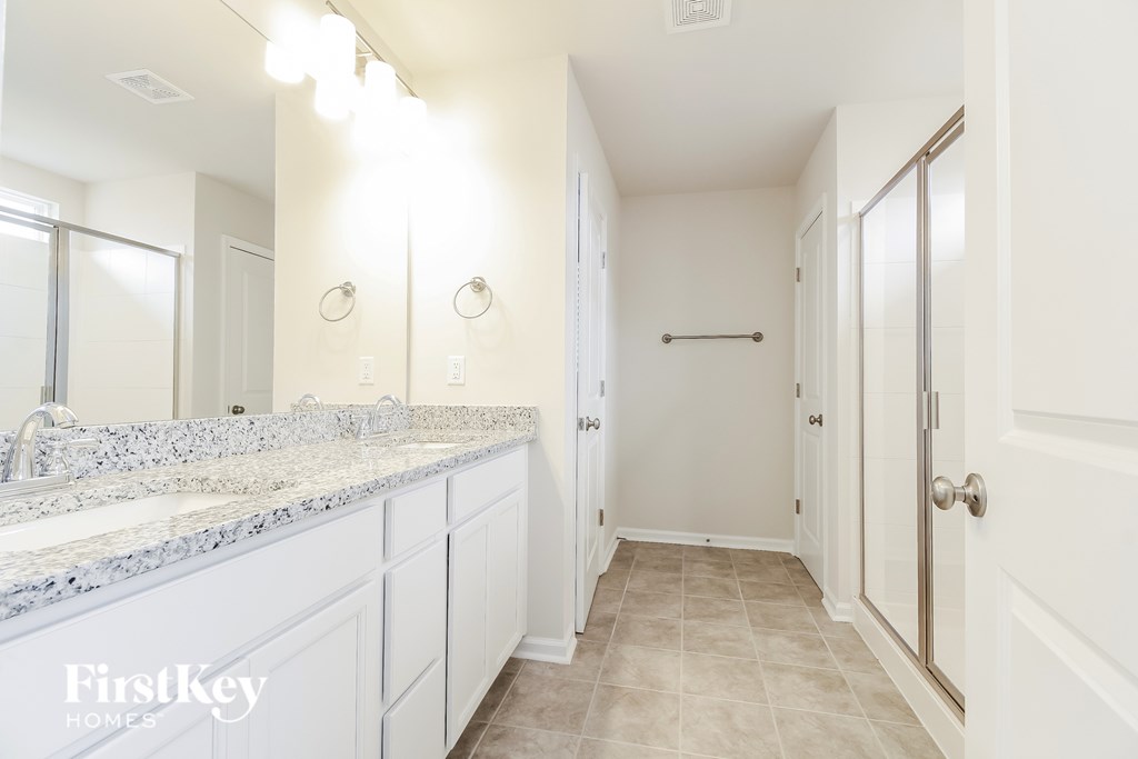 A white bathroom with a marble counter top and a walk in shower.