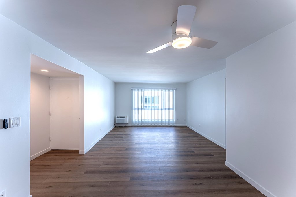 a living room with white walls and wood floors and a ceiling fan