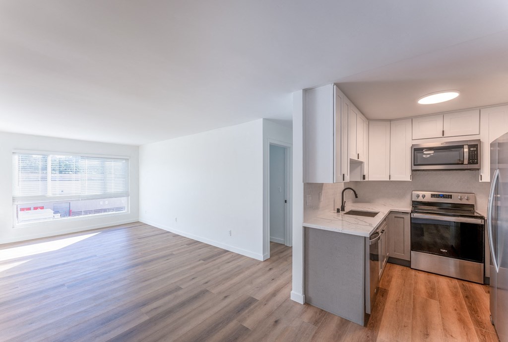 an empty living room with a kitchen with stainless steel appliances