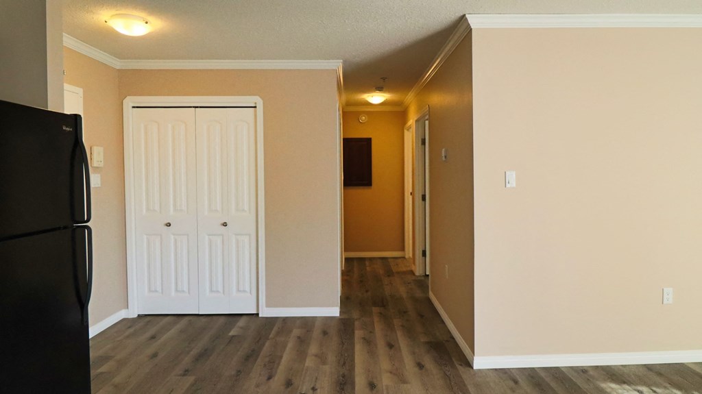 an empty living room with a refrigerator and a door to a hallway