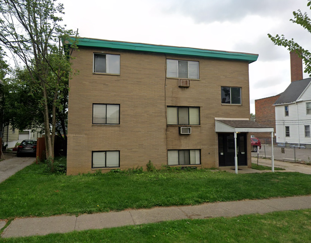A brown brick building with a green roof sits on a grassy lot.