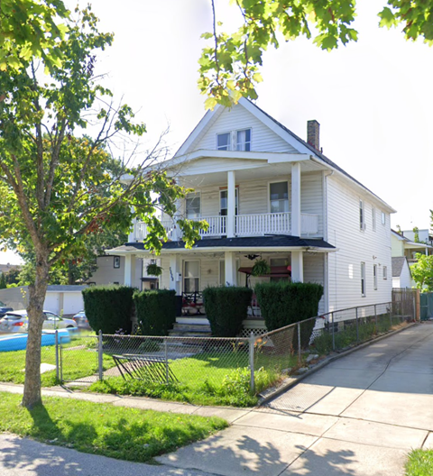 A white house with a porch and a tree in front.
