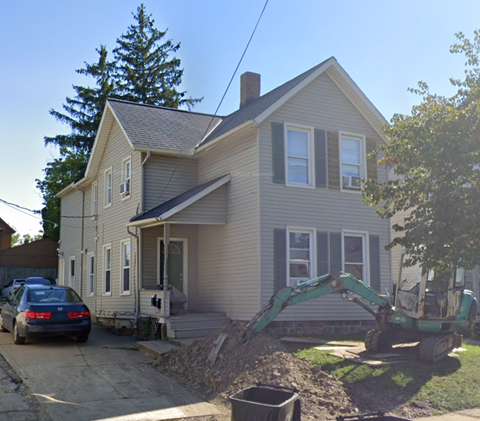 A house with a car parked in front and a construction vehicle in the yard.