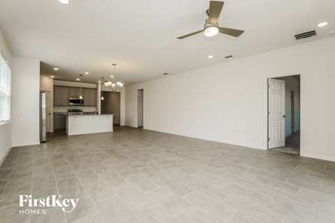 A spacious room with a ceiling fan and a kitchen area in the background.