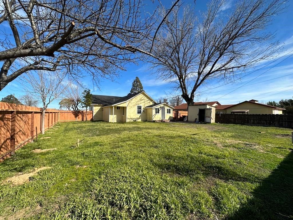 a backyard with a fence and a yellow house and a grassy yard