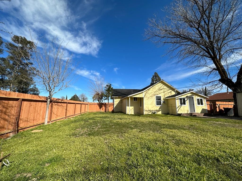 a backyard with a yellow house and a wooden fence