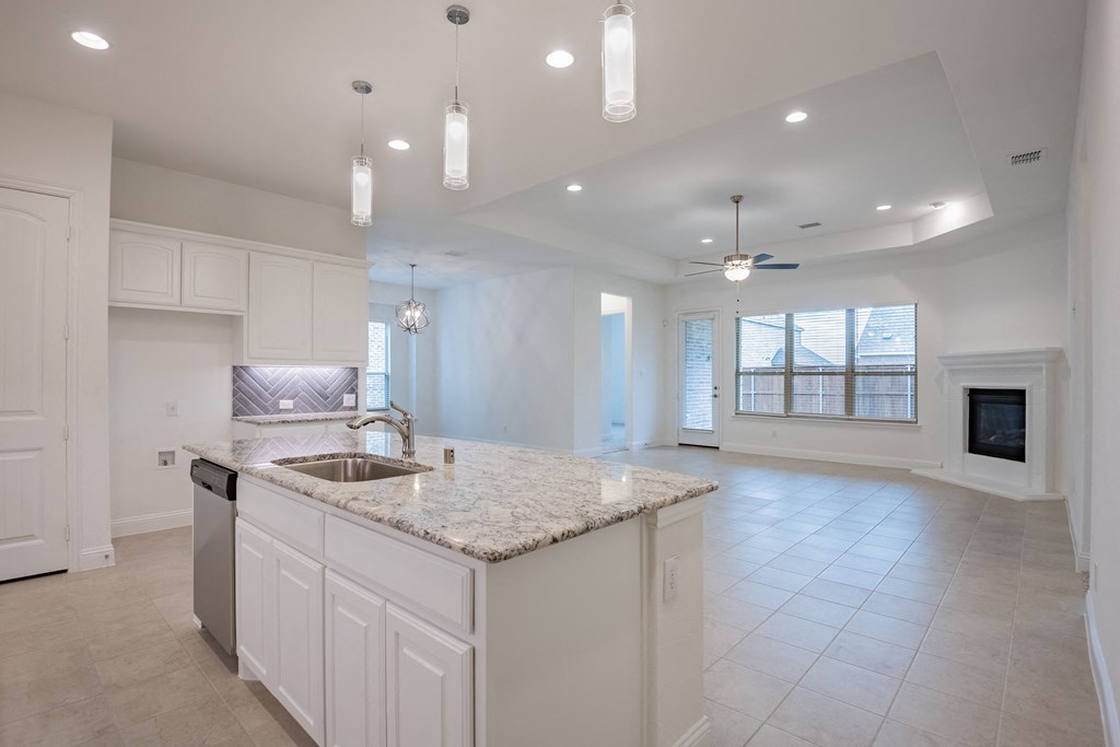 an open kitchen and living room with white cabinets and a marble counter top