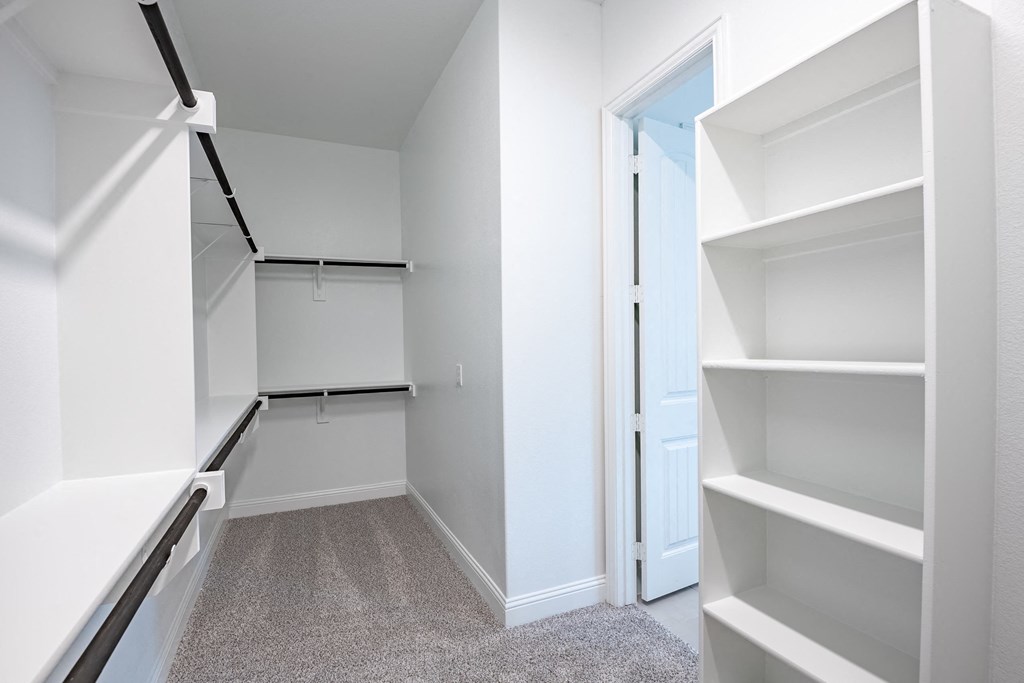 a walk in closet with white shelving and a white door