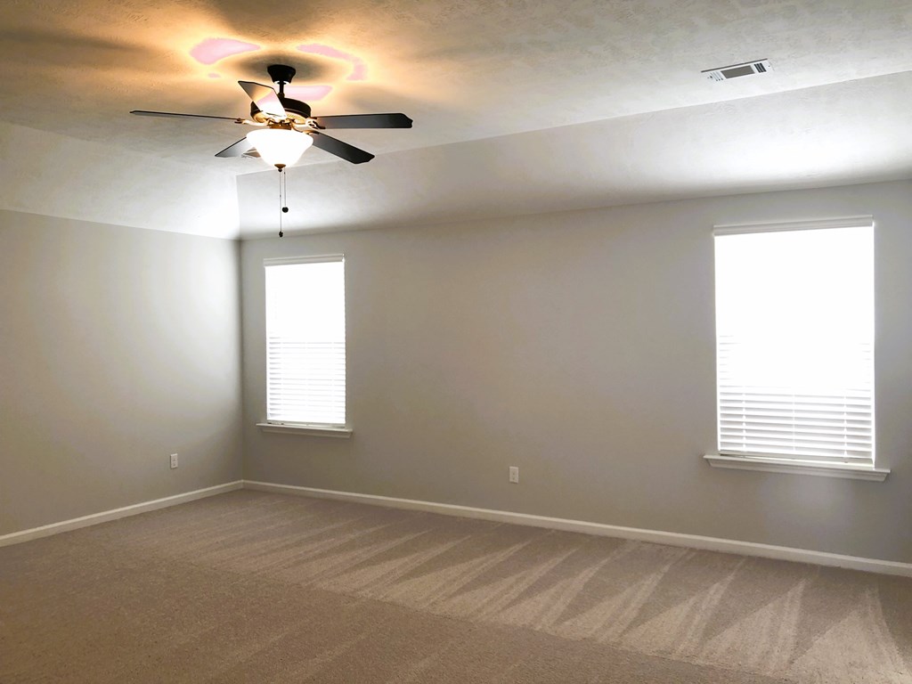 A room with a ceiling fan and two windows.