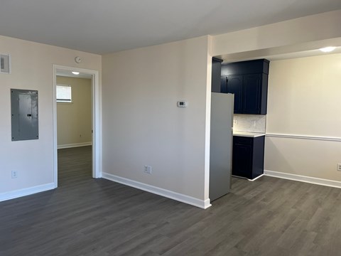 an empty living room and kitchen with a refrigerator and black cabinets