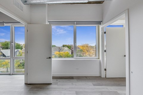 A room with white walls and a large window with a view of houses and trees outside.