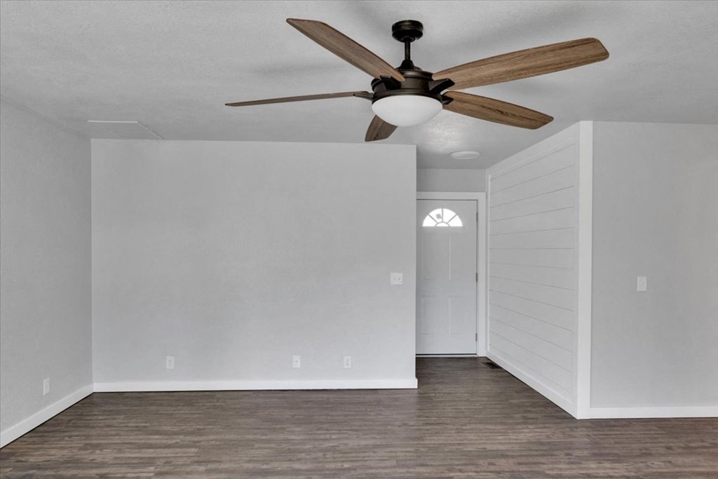 an empty living room with a ceiling fan and white walls
