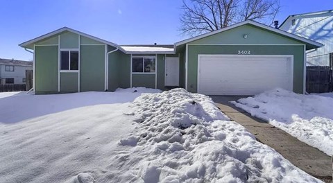 a green house with a driveway covered in snow