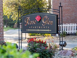 a sign for rose glen apartments in front of a gate with flowers