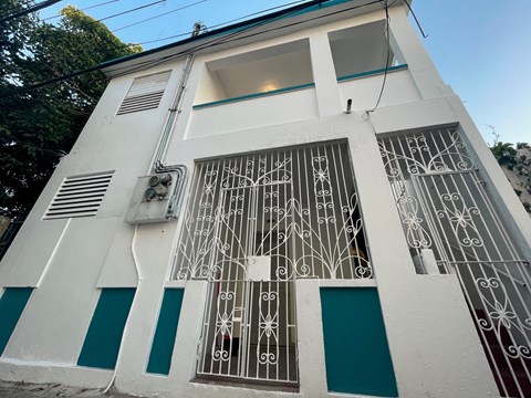 A white building with a blue stripe and a window with a decorative iron grill.