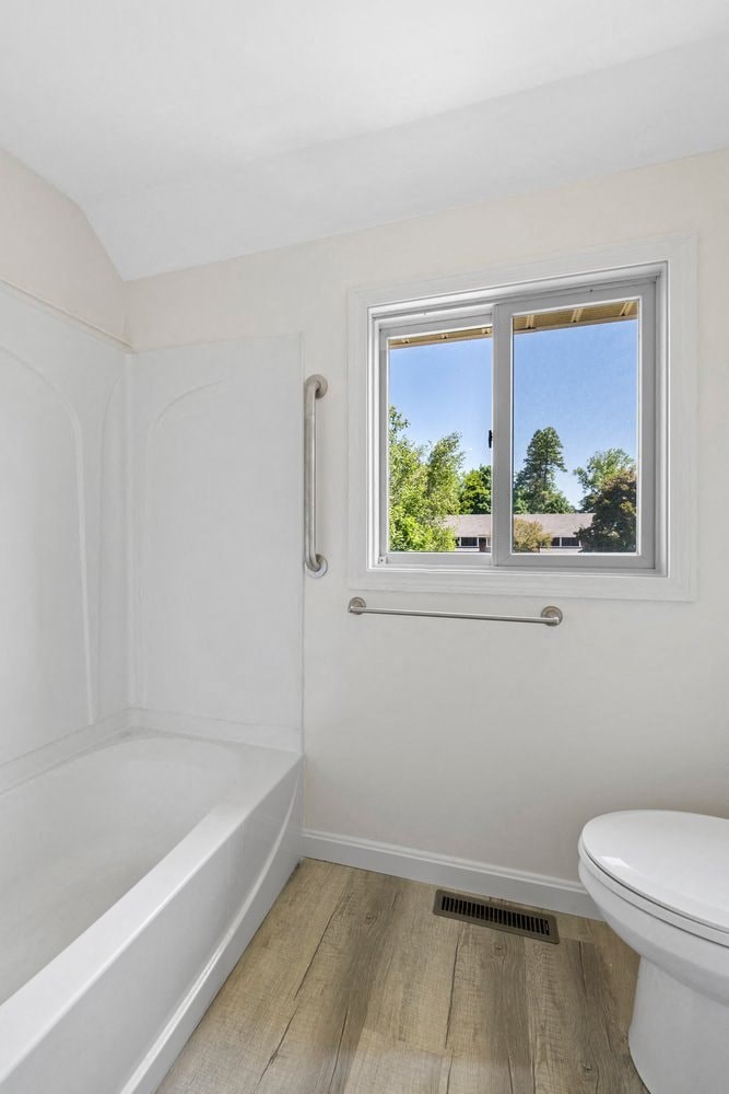 a white bathroom with a window and a toilet and a tub