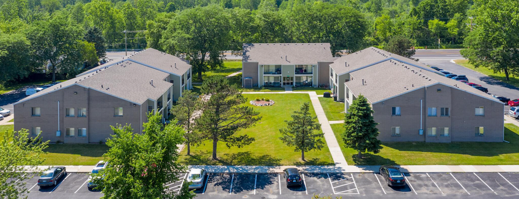 an aerial view of three buildings with a lawn and a parking lot