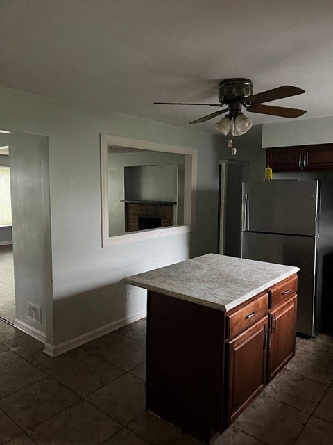 an empty kitchen with a refrigerator and a ceiling fan