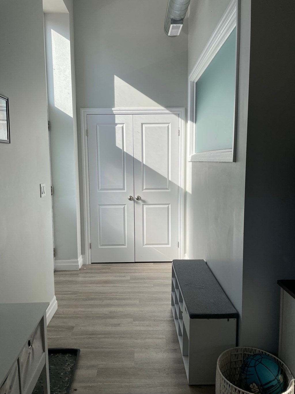 A white door is in a hallway with a bench and basket.