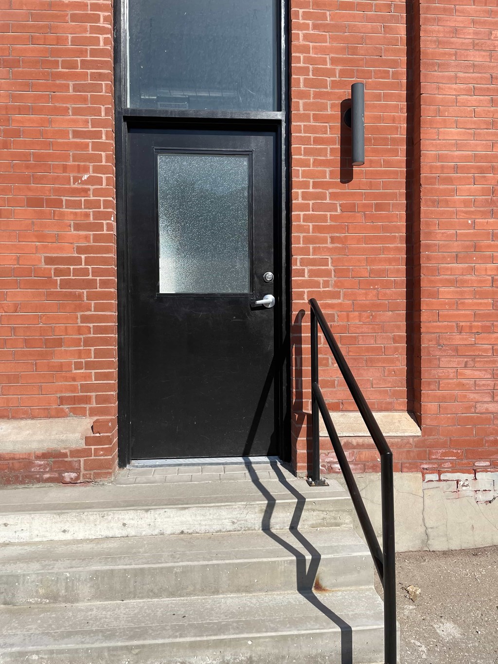 A black door with a glass window is set in a red brick wall.