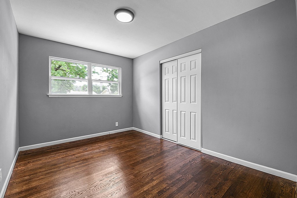 an empty bedroom with wood floors and a window
