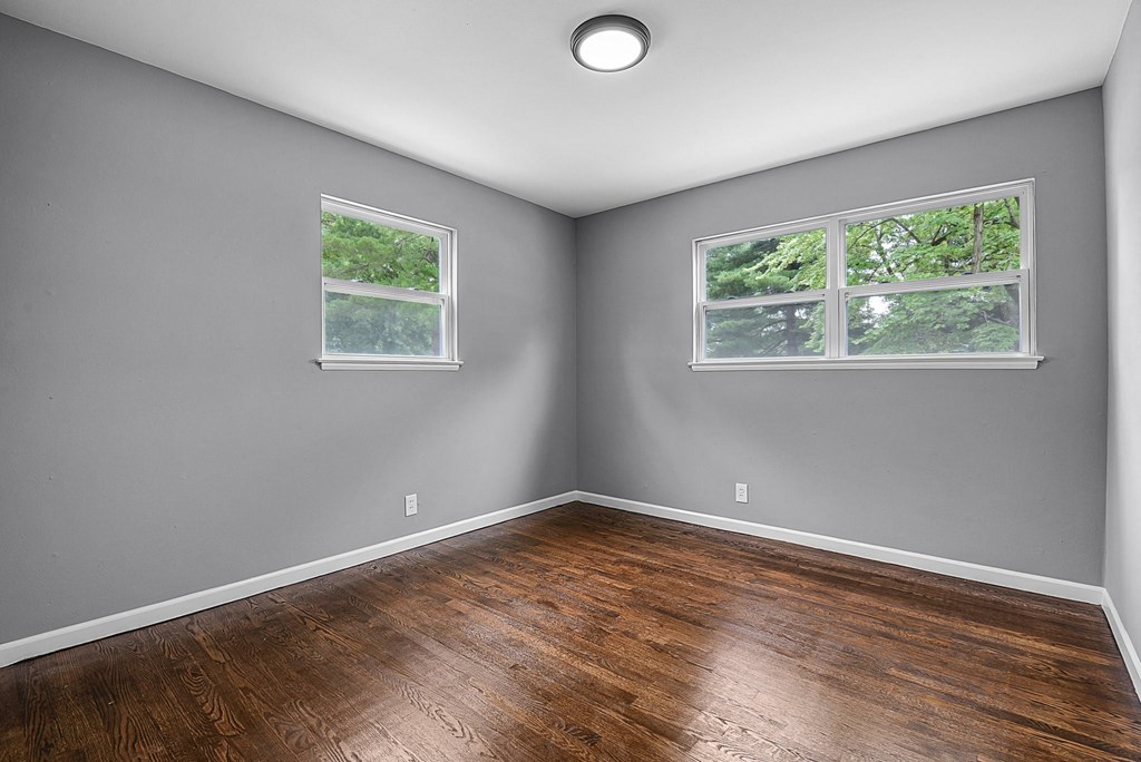 an empty room with wood floors and two windows