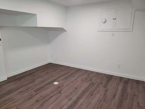 A room with wooden flooring and a white cabinet with a round object on the floor.
