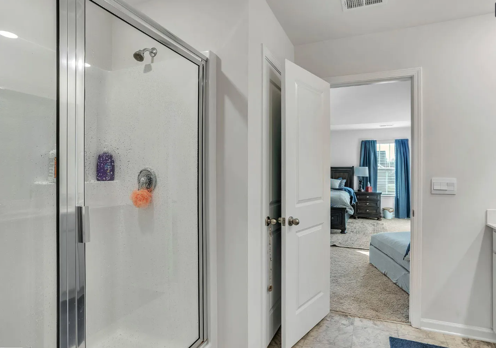 a bathroom with a glass shower and a door to a bedroom