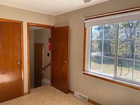 A room with a window and a view of a fence and trees outside.