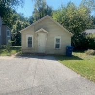 a small tan house with a white door and a driveway