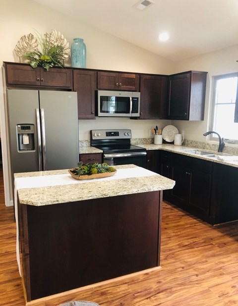 A kitchen with a refrigerator, microwave, oven, sink and wooden floors.